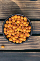 Juicy ripe orange sea buckthorn berries in bowl on wooden table, top view. Fruits of farm labor. Ingredients for dishes. Berries for freezing.