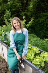 pretty blonde young woman posing in front of raised bed, vegetable patch in garden and is happy