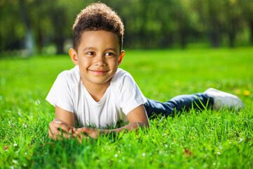  Little boy lies on green grass in a summer park