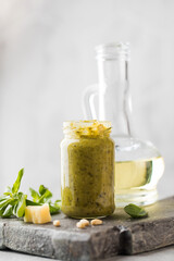 Pesto sauce with green basil leaves, slices of parmesan cheese and a jug of olive oil on a wooden board. Italian cuisine