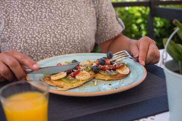 Mature woman with healthy summer breakfast, classic american pancakes with banana, kiwi, fresh berry and honey