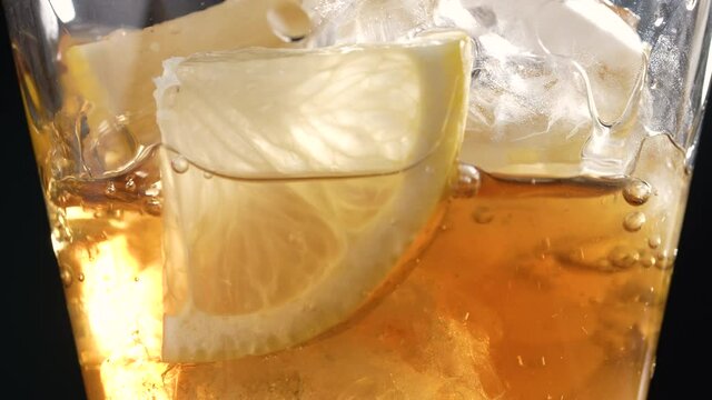 Pouring fresh Ice tea into glass glass with ice cubes, sliced lemons. Healthy refreshing lemonade for detoxification, sweet tasty soft drink or cold aromatic beverage for summer time in slow motion