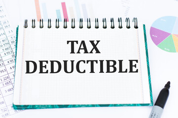 Tax deductible inscription on the notepad on the desktop next to the black marker and diagrams