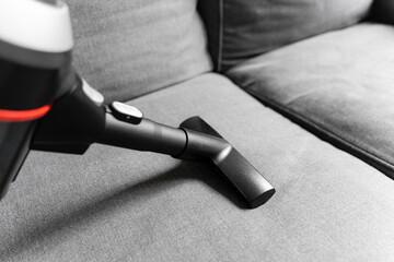 Cleaning grey sofa with wireless vacuum cleaner. Handheld cordless cleaner. Household appliance....