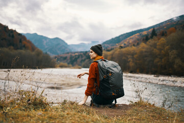 Fototapeta premium woman hiker on the banks of the river in autumn and mountains in the distance clouds weather nature