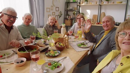 POV of cheerful senior friends smiling and waving at camera while talking selfie at home dinner - Powered by Adobe