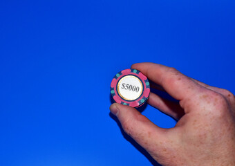 Poker chip for casino game in hand on blue background.