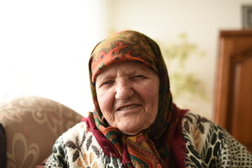 a very old woman in traditional Muslim clothes sitting in the house next to the window
