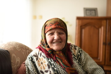 a very old woman in traditional Muslim clothes sitting in the house next to the window