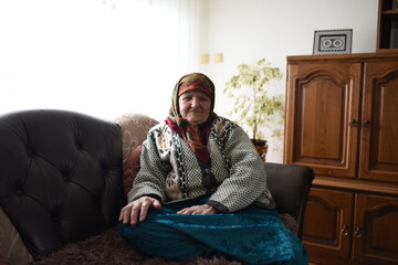 Fototapeta premium a very old woman in traditional Muslim clothes sitting in the house next to the window