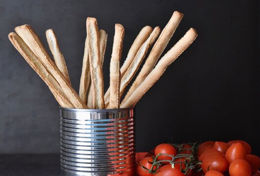 Gressini bread sticks in tin can and cherry tomatoes on black background