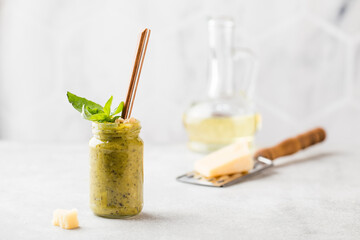 Homemade pesto sauce in a jar with a basil leaf, bottle of olive oil, a slice of parmesan and a spoon. Italian cuisine.