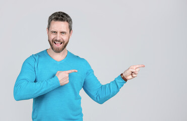 happy mature man with beard pointing finger on grey background with copy space, advertising