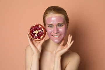 Young woman with pomegranate face mask and fresh fruit on pale coral background