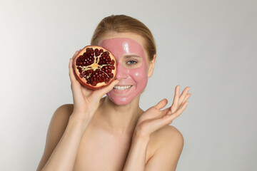 Young woman with pomegranate face mask and fresh fruit on light grey background