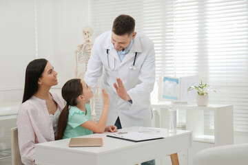 Mother with daughter visiting pediatrician in hospital. Doctor giving high five to little girl