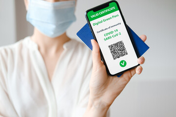 Unrecognized woman in mask holding smartphone with digital green pass and QR code on the screen....