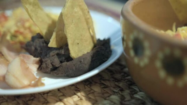 Mexican-style eggs, bacon, and refried beans with tortilla chips on white plate