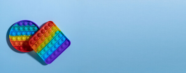 Anti-stress round and square rainbow colored toy Pop it on a blue background. There is a place for your text. A simple dimple. The child will play. shadow. Banner.