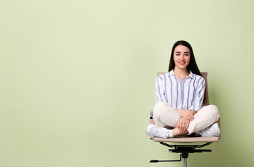 Young woman sitting in office chair on green background, space for text