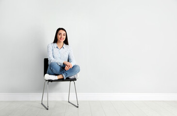 Young woman sitting on chair near white wall in office, space for text