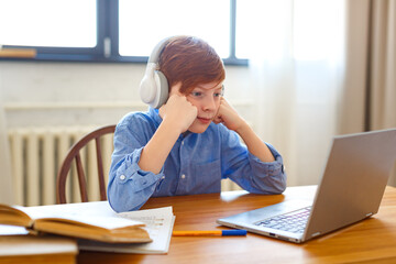 Photo of a student during an online lesson. He sits in headphones and listens to a boring lesson topic.