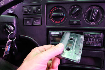 The driver inserts a cassette into a cassette recorder in an old car.