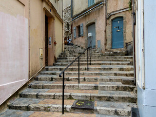 Fototapeta na wymiar Stairs in the old town of Cannes in France. Stairway to the residential houses in historic district of city. Scene with communication of young man and woman by mobile phones.