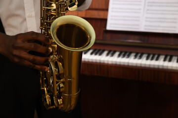 Obraz premium African-American man playing saxophone indoors, closeup with space for text. Talented musician