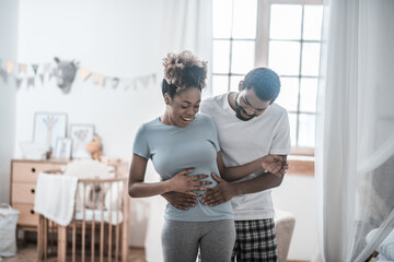 Fototapeta premium Happy man touching wifes belly with his palms