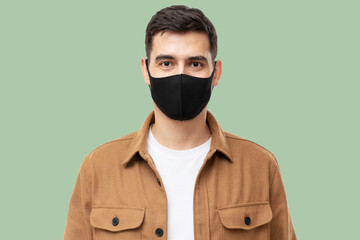 Young man wearing trendy brown workwear shirt and black face mask standing isolated on green background