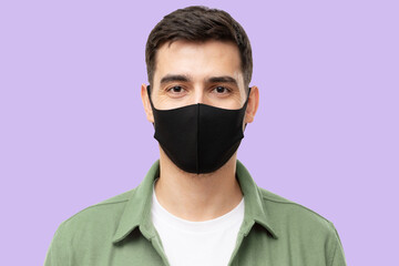 Portrait of young man wearing trendy green cargo shirt and black mask, isolated on purple background