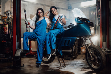Fototapeta na wymiar Two female mechanic posing next to a sportbike in authentic workshop garage