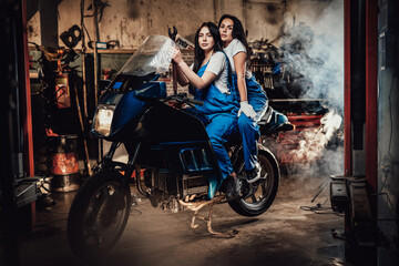 Obraz na płótnie Canvas Two female mechanic sitting on sportbike in authentic workshop garage