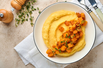 Polenta with butter, pumpkin, garlic, savory and parmesan cheese in white bowl on light concrete...