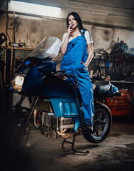 Fototapeta na wymiar Female mechanic relaxing smoking a cigarette while standing on sportbike in garage or workshop