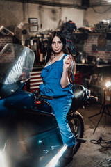 Obraz na płótnie Canvas Beautiful brunette female mechanic smoking a cigarette while sitting on sportbike in garage