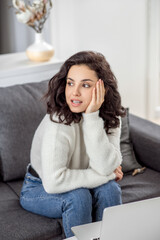 Fototapeta premium A young woman in a white sweater sitting on the sofa and looking aside