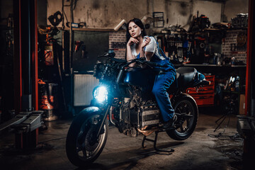Fototapeta na wymiar Beautiful brunette biker or mechanic relaxing smoking a cigarette in garage or workshop