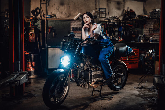 Beautiful brunette biker or mechanic relaxing smoking a cigarette in garage or workshop