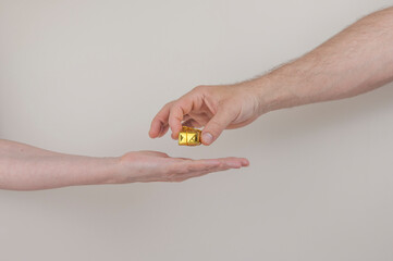 men holding a small gold ribbon wrapped gift box to female open hand on a white backdrop with copy space.