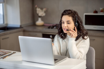 An operator in earphones sitting at the laptop while working from home
