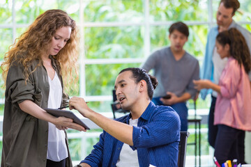 Focus handsome Caucasian male boss teaching, explaining, giving advice to hipster trendy creative female subordinate in comfortable modern office with profession and background of diverse staff.