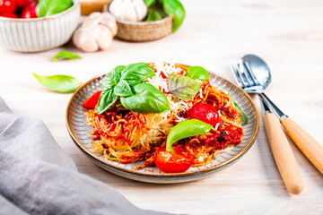 Italian pasta with tomato sauce, tomatoes, cheese and basil on a light table