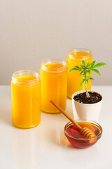 Three jars of CBD honey, a marijuana plant and honey in a bowl
