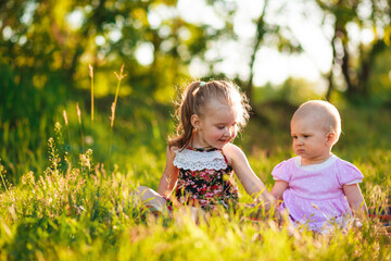 1 and 3 years old girls are sitting on the green grass and. Nature in the village.