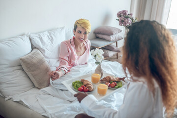 Obraz na płótnie Canvas Happy woman in bed and girlfriend with breakfast