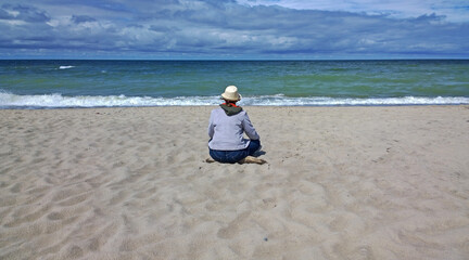 Rear view of woman sitting on the beach and looking at the sea