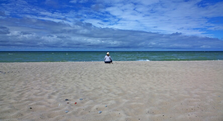 Rear view of woman sitting on the beach and looking at the sea