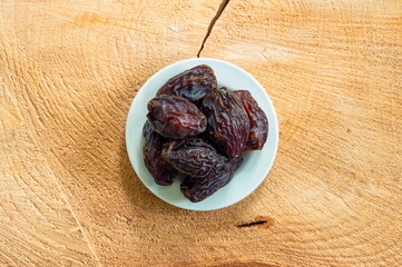 Big pitted dried dates on a small white plate set on a wooden boar top view